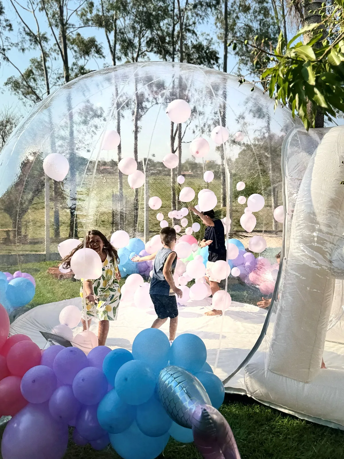 Crianças brincando dentro da Bubble Dream House cercadas de balões brancos flutuantes