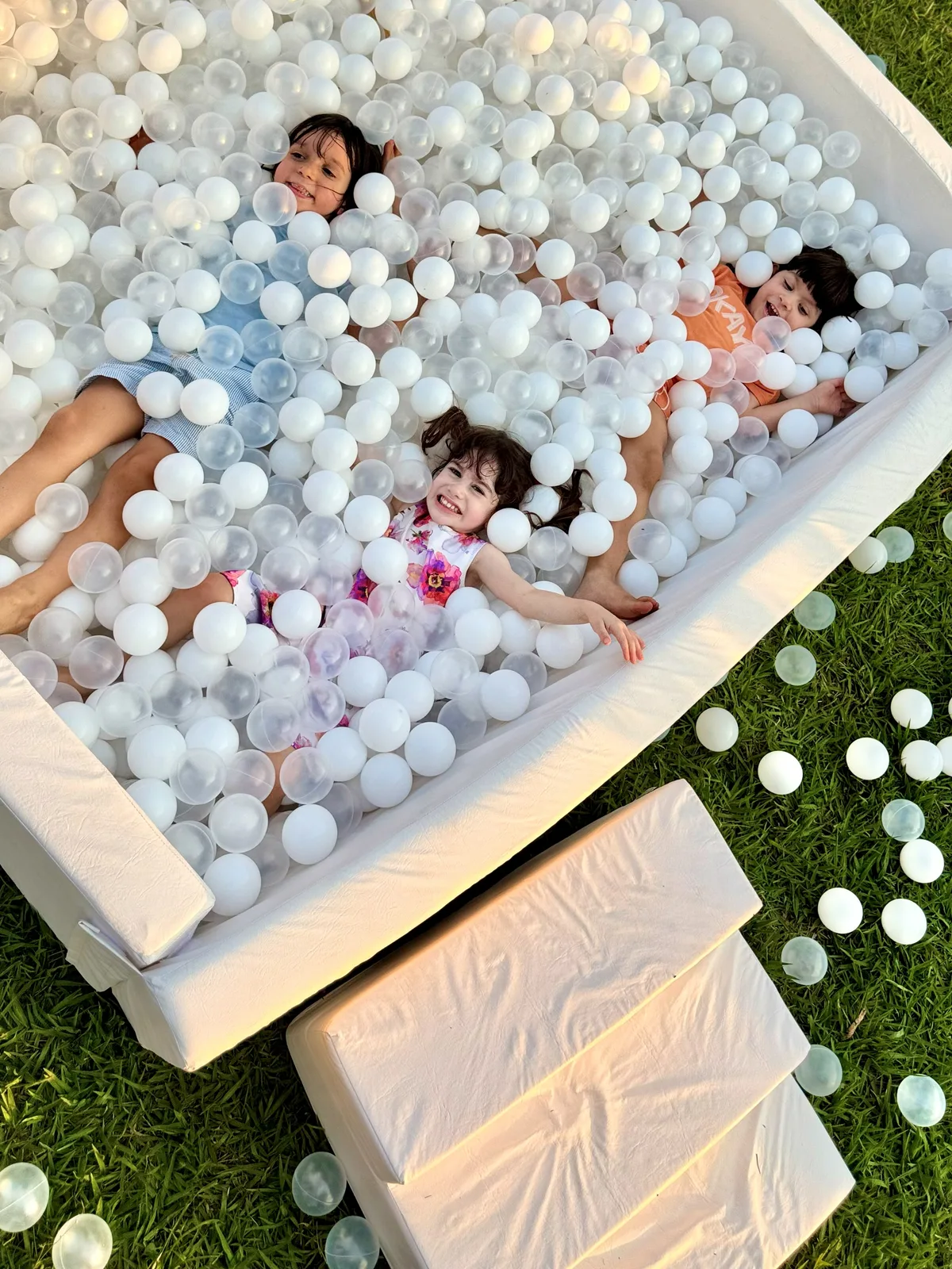 Crianças deitadas e sorrindo na piscina de bolinhas branca da Slide Pool